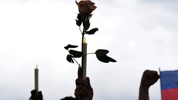 A hand holding up a candle and flower next to a Haitian flag